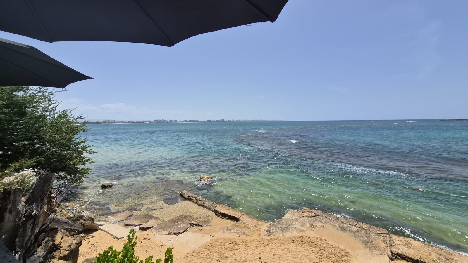 Clear turquoise water over flat coastal rock, with the city far across the bay
